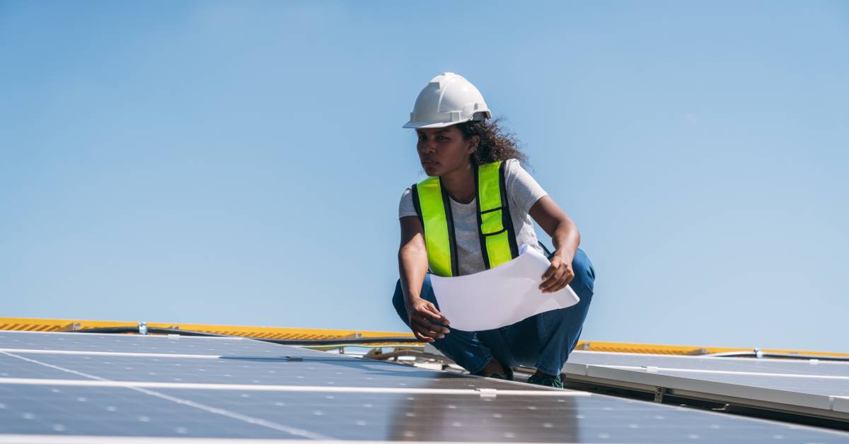 A maintenance worker is looking for damaged parts in a solar panel system. She is holding the schematic for reference.