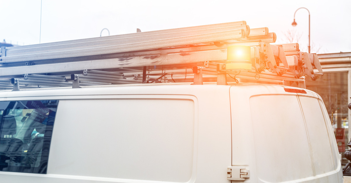 A white service truck with a metal ladder on the top of the vehicle. It is parked outside of a residential home.