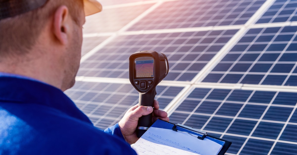 A technician taking data of a solar field in front of him. He is recording the external temperature with a thermal camera.