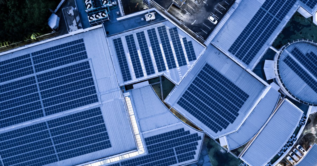 An aerial view of a commercial building with solar panels installed on the roof. There is a parking garage near the roofing.