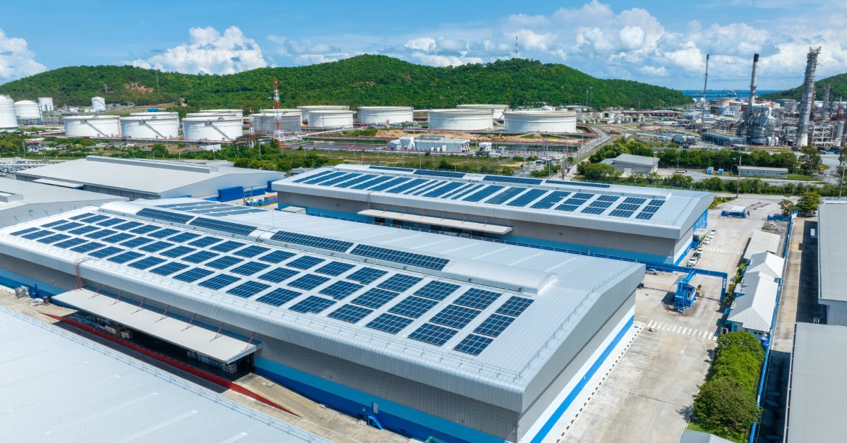 An industrial building with solar panels installed on the roof. There are other industrial buildings surrounding the area.