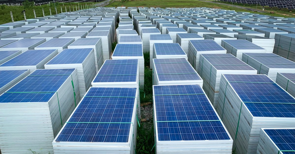 Numerous solar panels in a field stacked on top of each other and tied together with a green plastic rope.