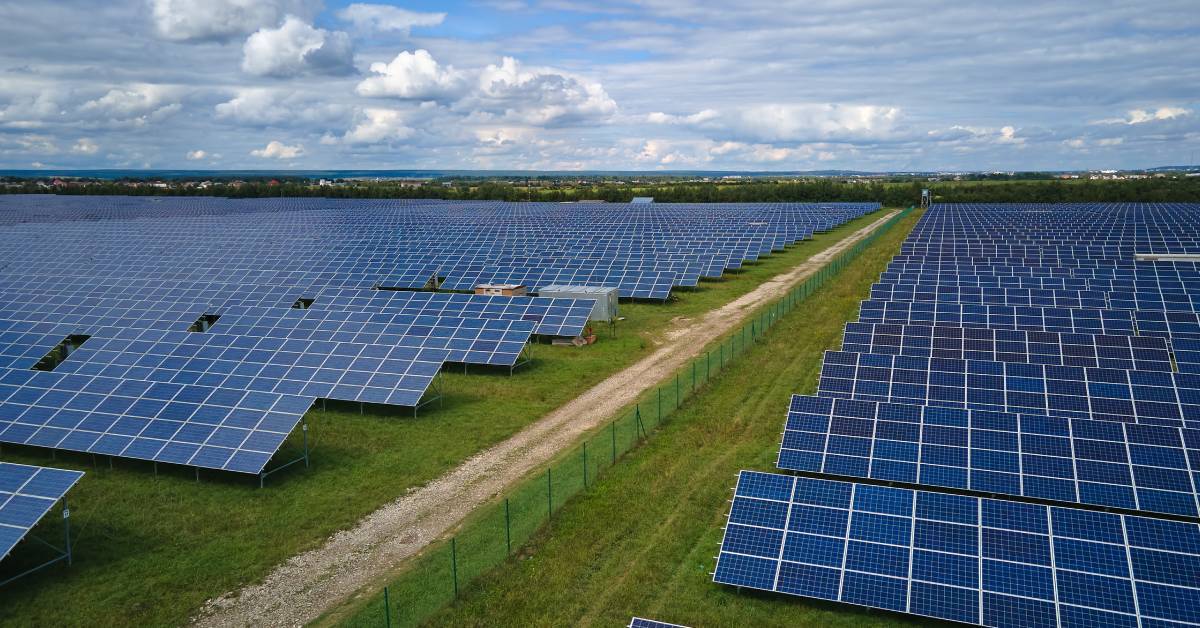 A solar grid separated by a green fence and a cobblestone path. There is equipment located in the middle of the grid.