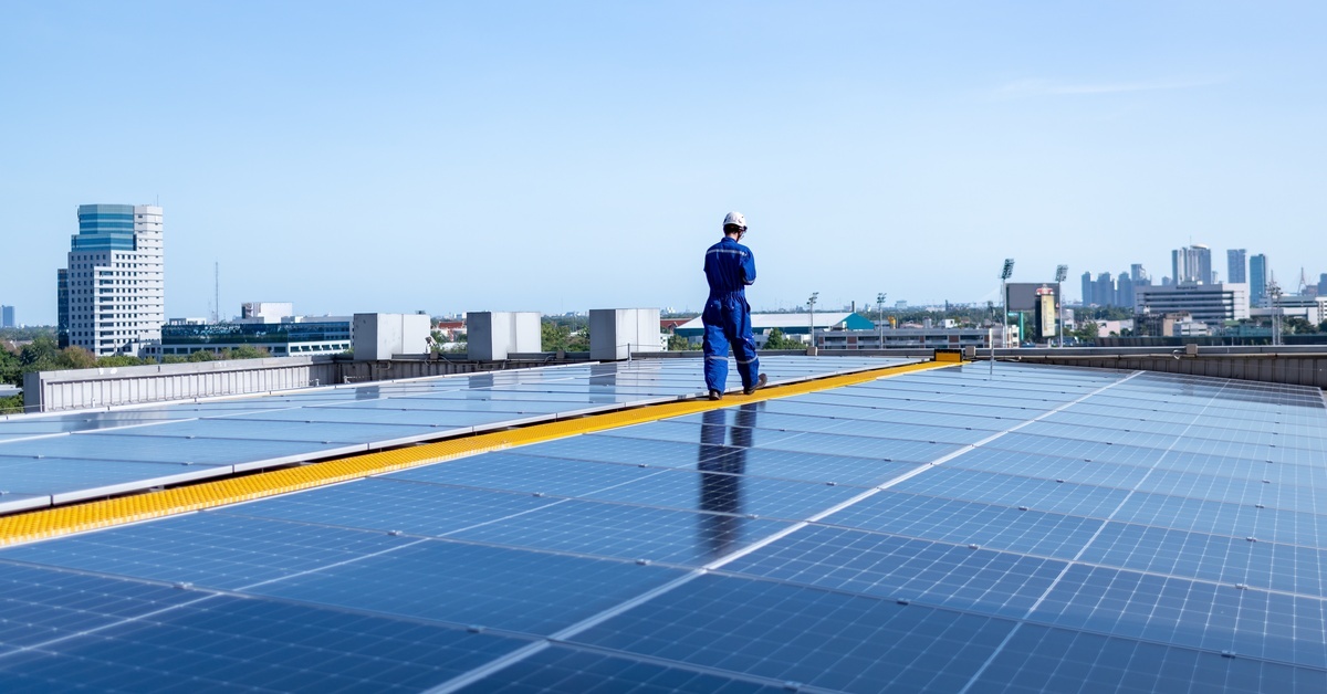 An expansive solar grid installed on the roof of a building. There is a solar worker walking between the panels.