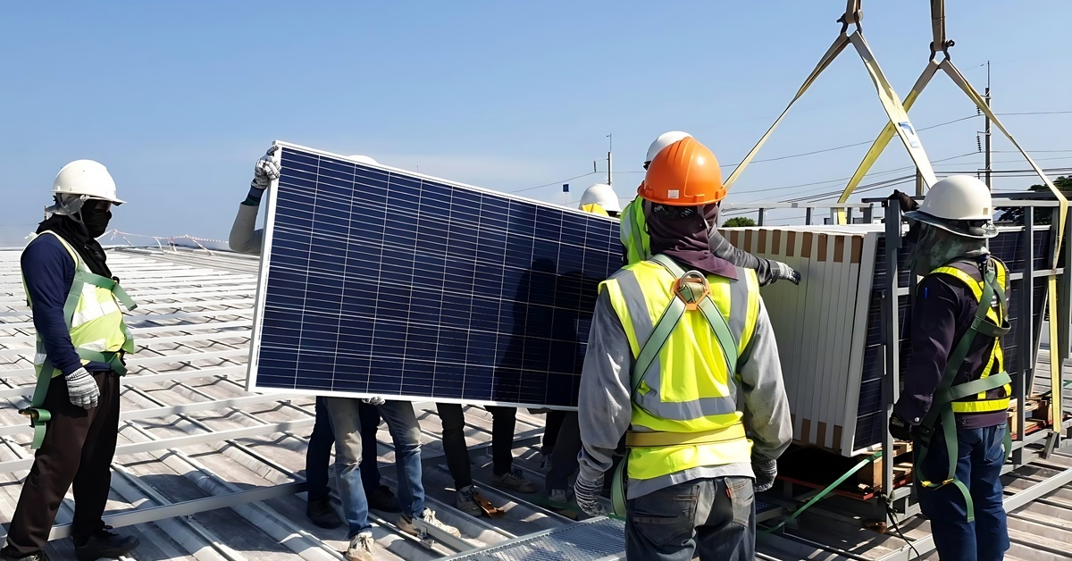 Solar engineers standing on the roof of a building. Some of them are lifting a solar panel from a stack.