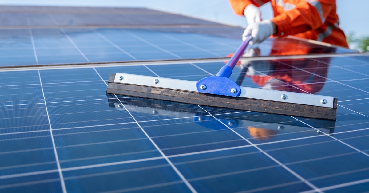 A person using a squeegee on a solar panel. They are wearing white gloves and a reflective orange shirt.