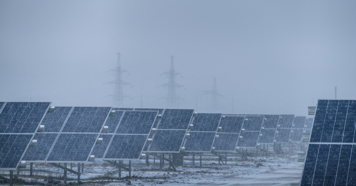Large rows of solar panels that are being used by a power plant surrounded by snowy weather conditions.