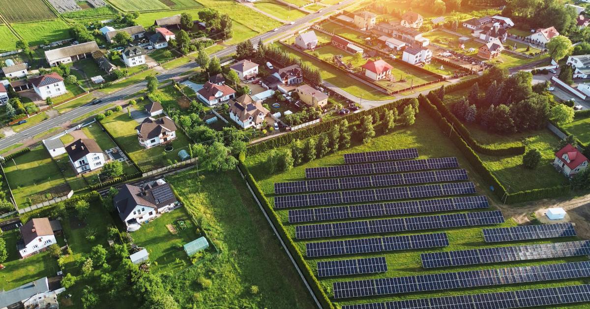 A field of solar panels absorbing sunlight next to a neighborhood. The neighborhood houses use renewable energy.