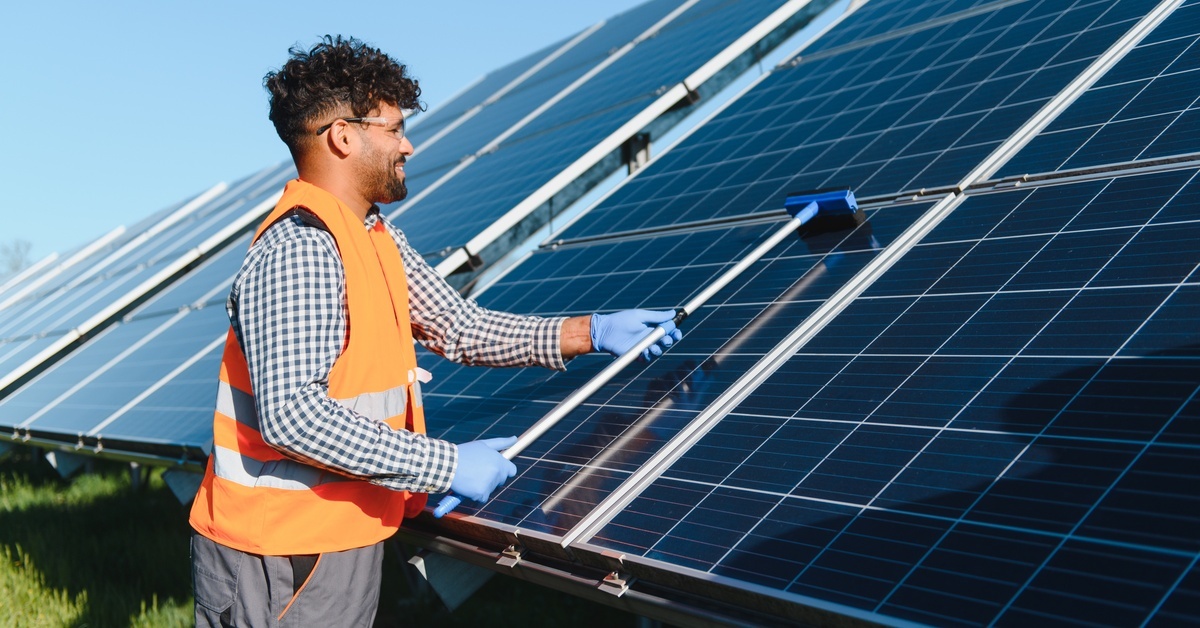 8 Tips for Solar Panel Maintenance and Cleaning An engineer cleaning a panel on a solar farm with a specialized tool. The engineer is wearing a high-visibility vest.