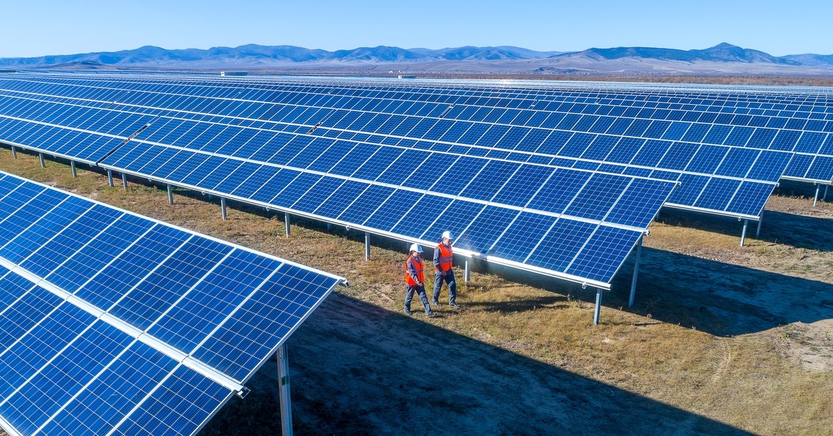 A solar power station with rows of solar panels set up facing the sun. Workers are walking through a row of panels. A solar power station with rows of solar panels set up facing the sun. Workers are walking through a row of panels.