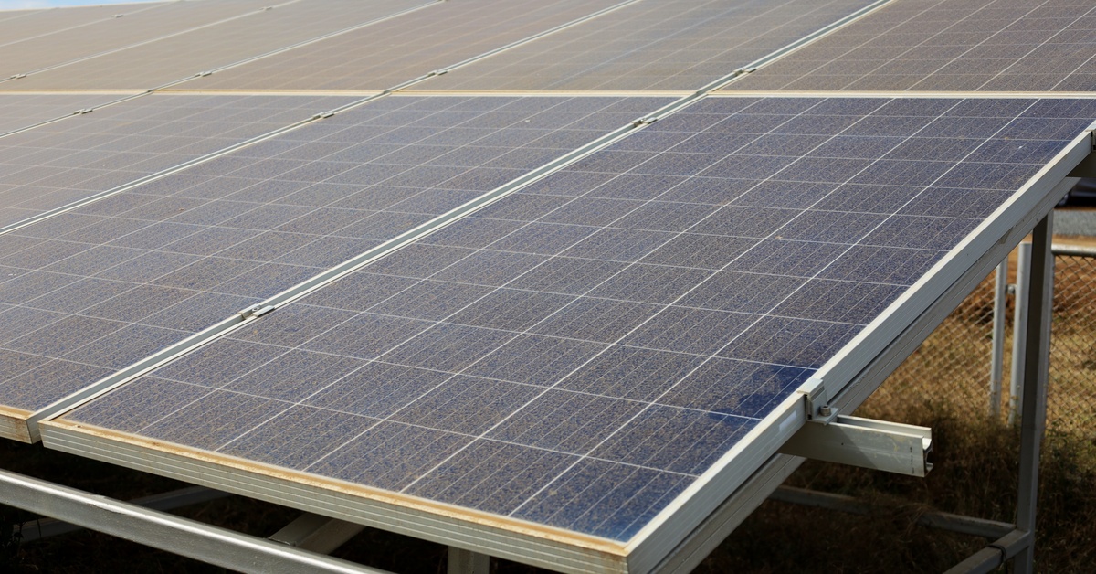 Solar panels on a sunny day with dust covering them. The thin layer of brown dust obscures part of the panels.