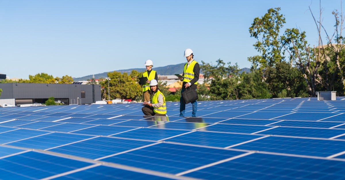 A team of engineers sitting or standing in the middle of rows of solar panels with devices to analyze power performance.