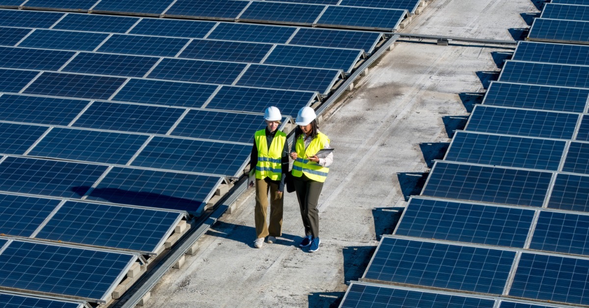 Engineers in safety gear walking between rows of solar panels on the roof. They are inspecting the panels.