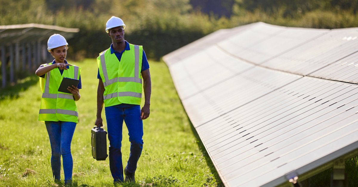 Choosing Between Engraved and Printed Solar Labels A man and woman wearing hard hats and safety vests inspecting rows of solar panels together in a grassy field.